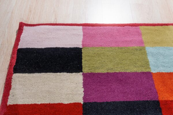 Colorful high-pile rug with geometric blocks of fuchsia, black, green, and beige on light flooring.