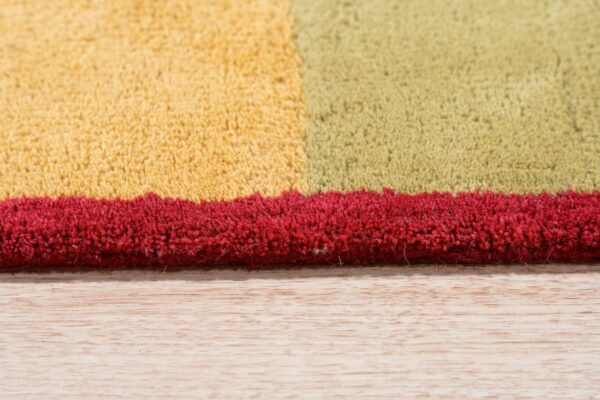 Close-up of a high-pile rug edge showing blocks of yellow, olive, and bright red on light wood flooring.