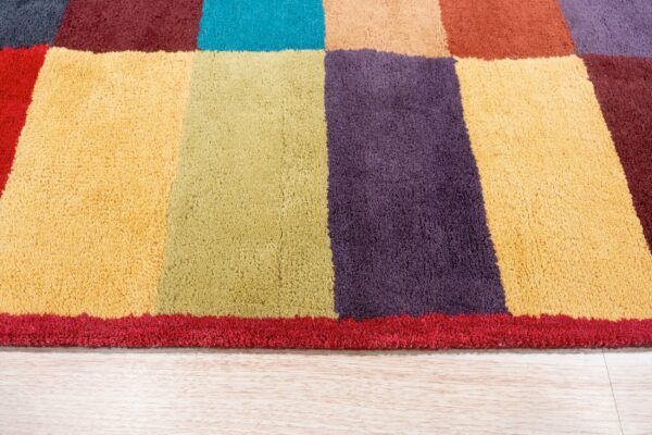 Multi-colored plush area rug featuring large blocks of yellow, purple, and green on light wood flooring.
