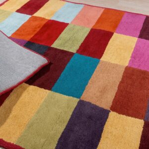 Multi-colored patchwork rug with plush texture on a light wood floor, exposing the woven gray backing.