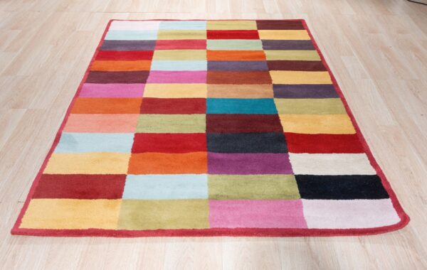 Vibrant geometric rug with staggered multicolored blocks sits on light blonde wood flooring.