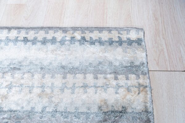 Corner of a soft pile rug displaying repeating light gray and ivory geometric shapes on blonde wood floor.