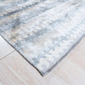 Abstract blue, gray, and beige rug corner with visible medium pile texture on light wood-look flooring.
