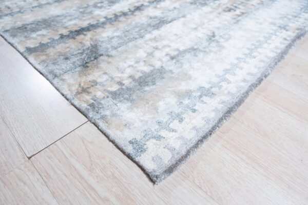Abstract blue, gray, and beige rug corner with visible medium pile texture on light wood-look flooring.