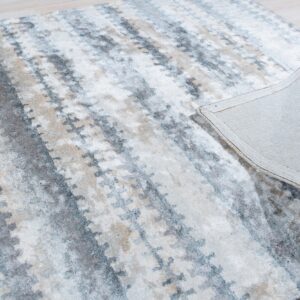 Abstract gray, cream, and tan rug folded back to show the backing on pale wood floor.
