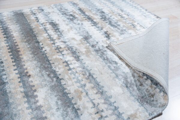 Abstract gray, cream, and tan rug folded back to show the backing on pale wood floor.