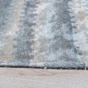 A soft pile rug with mottled gray and beige abstract patterns lies on light wood flooring.