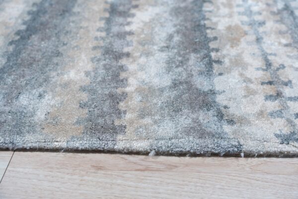 A soft pile rug with mottled gray and beige abstract patterns lies on light wood flooring.