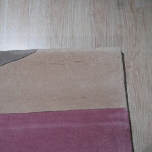 Plush rug detail showing color blocks of gray, tan, and pink against light wooden floors.