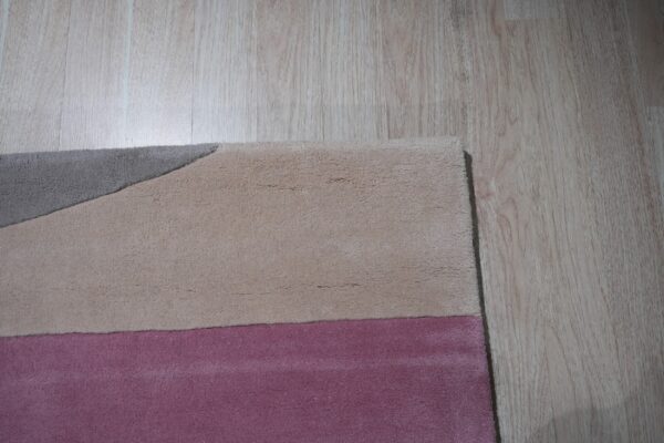 Plush rug detail showing color blocks of gray, tan, and pink against light wooden floors.