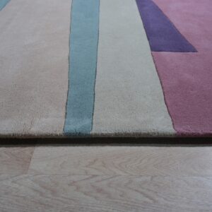 Plush rug featuring geometric blocks in beige, blue, lavender, and pink on light wood flooring.