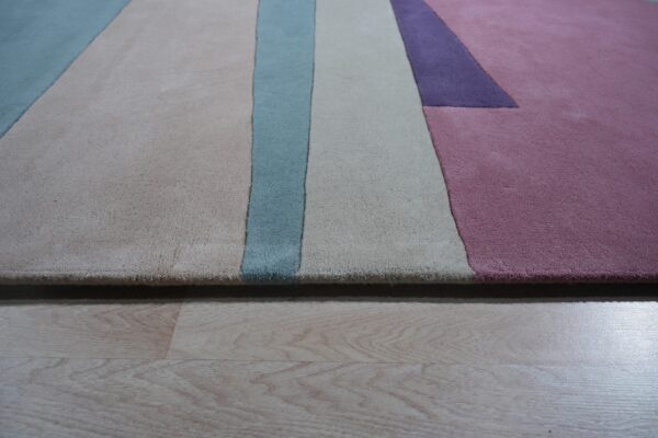 Plush rug featuring geometric blocks in beige, blue, lavender, and pink on light wood flooring.