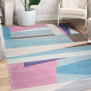Pastel pink, blue, purple, and brown geometric rug on wood floors next to a cream chair and plant.