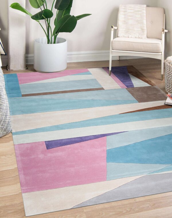 Pastel pink, blue, purple, and brown geometric rug on wood floors next to a cream chair and plant.