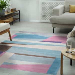Geometric rug in blue, pink, purple, and brown lies on light flooring beneath a beige sofa and wooden chair.
