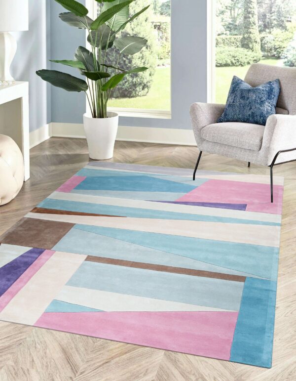 Abstract pink, blue, and brown low-pile rug on wood floors by a window and gray armchair.