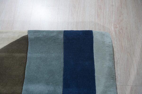 Medium pile rug featuring geometric blocks of deep blue, teal, gray, and brown on light wood floors.