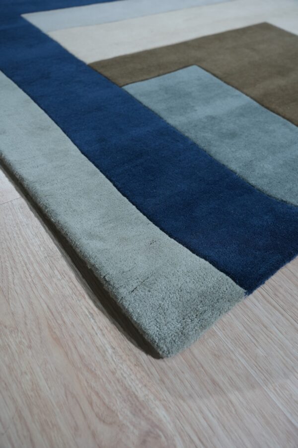 High-pile rug featuring geometric color blocks of navy blue, sage, brown, and cream on light wood flooring.