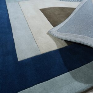Close-up of a deep blue and multicolored geometric block rug curled back, revealing its light woven backing.