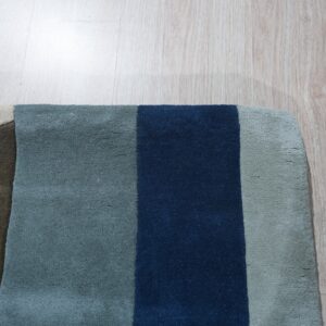Navy, blue, gray, olive, and tan color blocks define this low pile rug on light wood flooring.