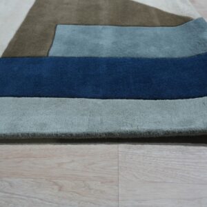 Close-up of a high-pile geometric rug in navy, slate, brown, and cream on light wood planks.