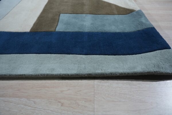 Close-up of a high-pile geometric rug in navy, slate, brown, and cream on light wood planks.