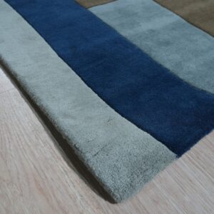 Thick pile rug featuring geometric blocks of deep blue, gray, beige, and brown on light wood flooring.