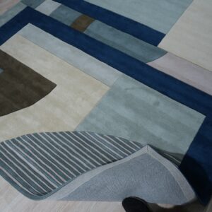 Abstract rug displaying large blocks of navy, teal, beige, and brown with striped accents on wood floor.