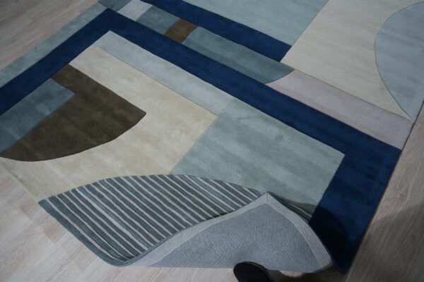 Abstract rug displaying large blocks of navy, teal, beige, and brown with striped accents on wood floor.