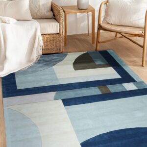 Blue, navy, and beige abstract geometric rug lies on wood flooring beside wicker and rattan furniture.