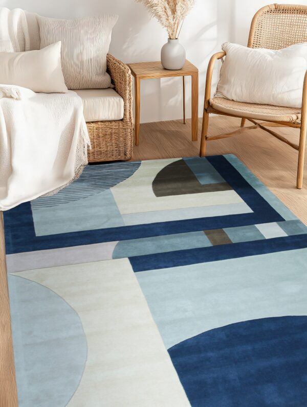 Blue, navy, and beige abstract geometric rug lies on wood flooring beside wicker and rattan furniture.