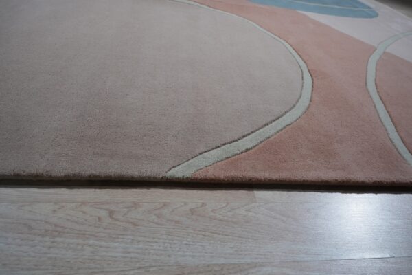 Abstract high-pile rug in blush, taupe, and light blue with carved curved lines on light wood floor.