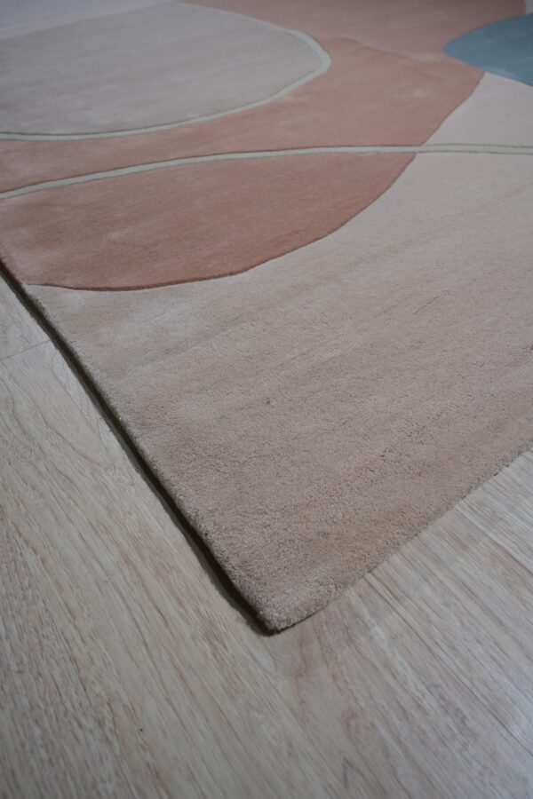 A low-pile rug featuring soft abstract pink, beige, and slate blue shapes rests on light wood flooring.