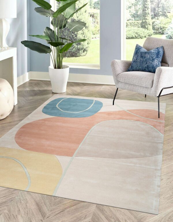 Abstract rug with blush, light blue, and yellow shapes on chevron wood flooring in a bright sunlit room.