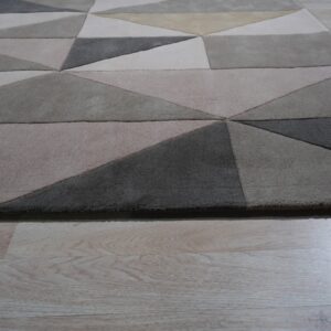 Low pile rug featuring a geometric pattern in shades of gray, beige, and tan on light wood flooring.