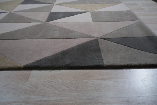 Low pile rug featuring a geometric pattern in shades of gray, beige, and tan on light wood flooring.