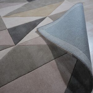 Geometric rug in varied neutral grey and beige shades shown on light wood flooring with the corner curled.