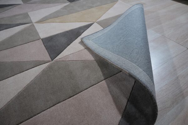 Geometric rug in varied neutral grey and beige shades shown on light wood flooring with the corner curled.