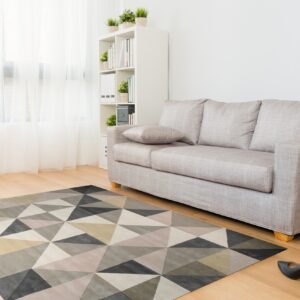 Geometric rug in varied gray, beige, and neutral triangles sits on wood floor beneath a light sofa.