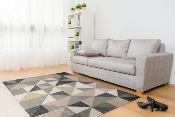 Geometric rug in varied gray, beige, and neutral triangles sits on wood floor beneath a light sofa.