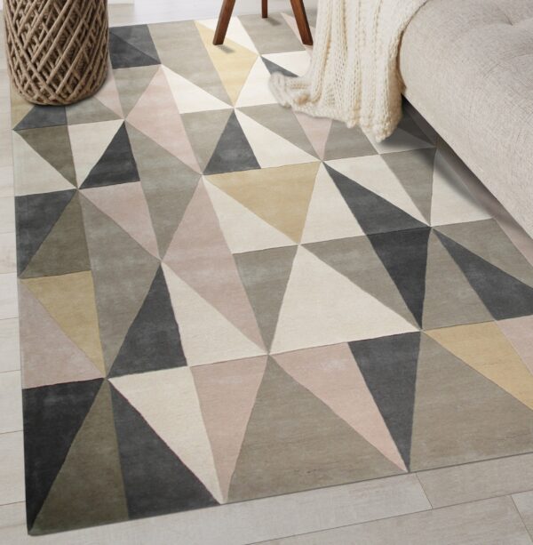 Geometric rug in gray, beige, and blush triangles placed on light plank flooring with neutral furniture.