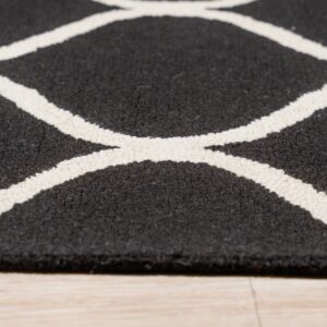 Low angle shot of a textured black and white geometric rug resting on light hardwood flooring.