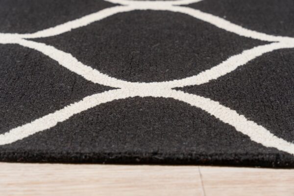 Low angle shot of a textured black and white geometric rug resting on light hardwood flooring.