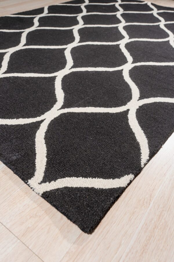 Black, textured rug with bold off-white trellis pattern on a pale wood floor.