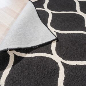 Black and cream geometric rug with medium pile rolled back on a light plank wood floor.
