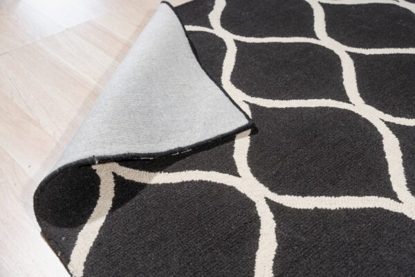 Black and cream geometric rug with medium pile rolled back on a light plank wood floor.
