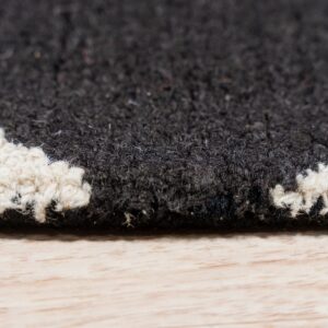Close-up of a black and white shag rug edge with a geometric pattern resting on light hardwood flooring.