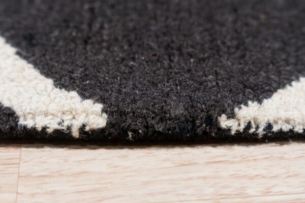 Close-up of a black and white shag rug edge with a geometric pattern resting on light hardwood flooring.