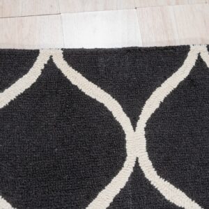 Close-up of a high-pile dark gray rug featuring a thick off-white geometric trellis pattern on light wood flooring.