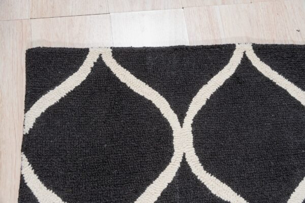 Close-up of a high-pile dark gray rug featuring a thick off-white geometric trellis pattern on light wood flooring.